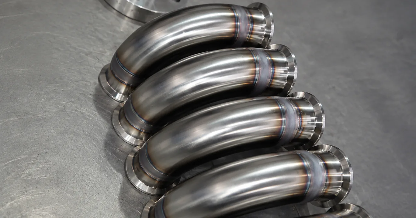 Five polished metal pipe bends stacked together.